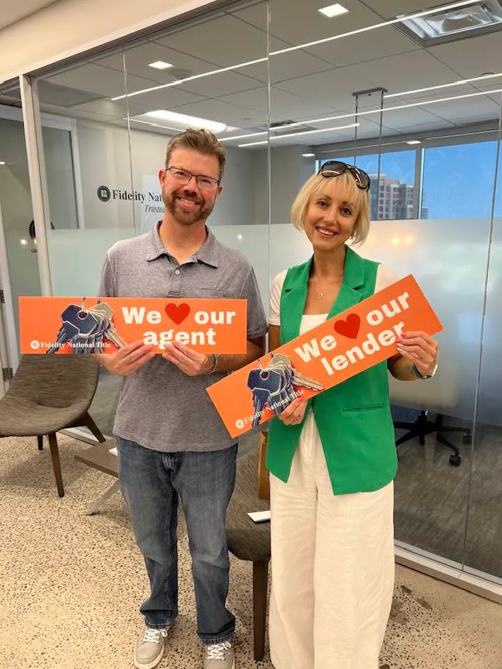 Client holding a "We love our agent" sign next to Tamila Aspen holding "We love our lender" at the title company